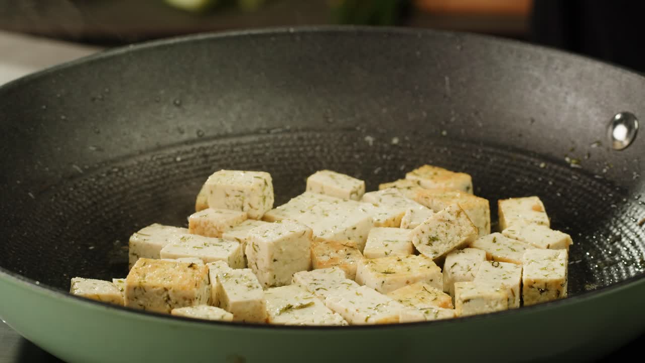 Fried tofu with sesame seeds and spices on cast iron pan, cooking japanese salad. Healthy ingredient for cooking vegan vegetarian diet food. Roasted tofu over black background.