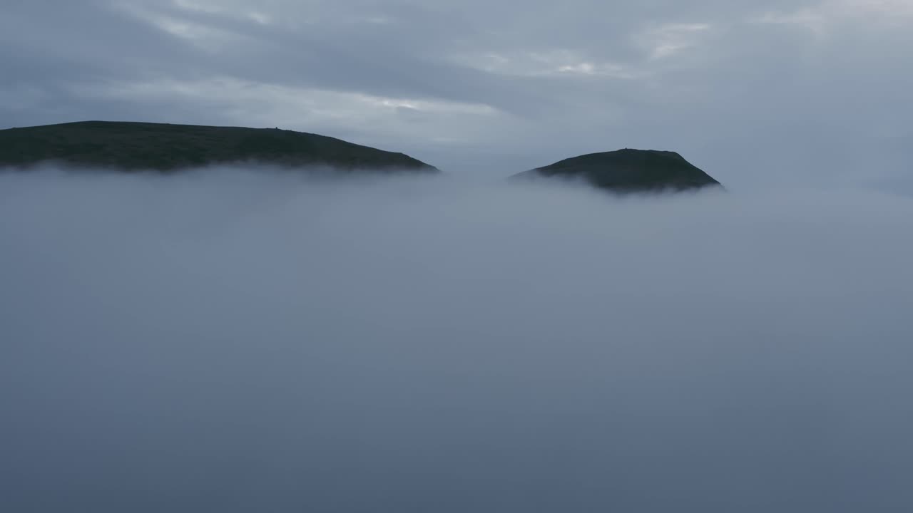 The camera emerges from the thick clouds, a view of a mountain peak