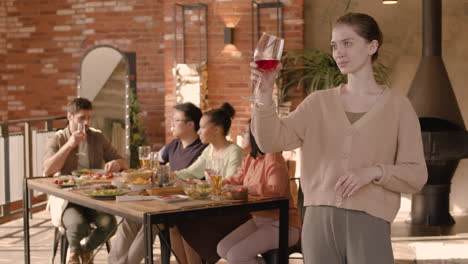 a red head young woman checking her glass of wine at a dinner party