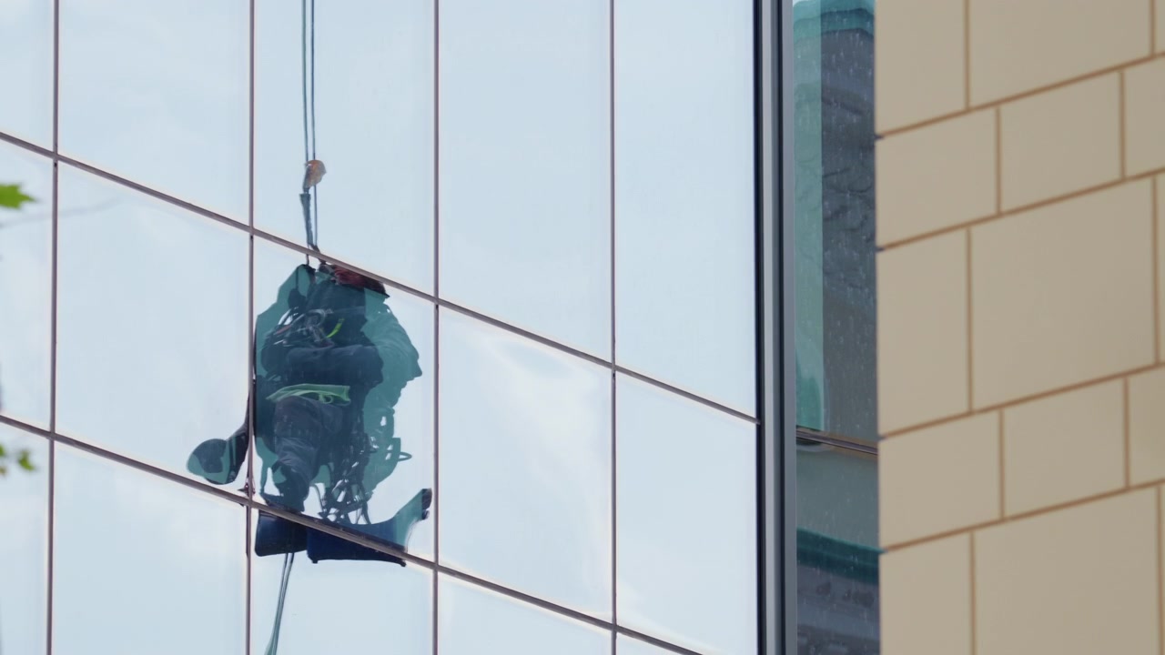 Riflesso di un lavavetri sospeso visibile sulla facciata in vetro di un moderno edificio per uffici