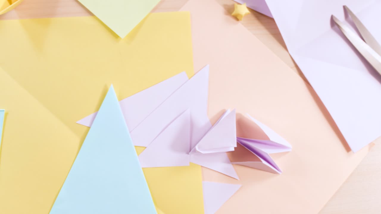 Foto dall’alto di carta origami color pastello, gru piegate e forbici su una scrivania di legno