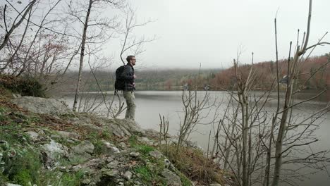 a man walking down to place his backpack on the ground next to the edge of the lake in slovenia