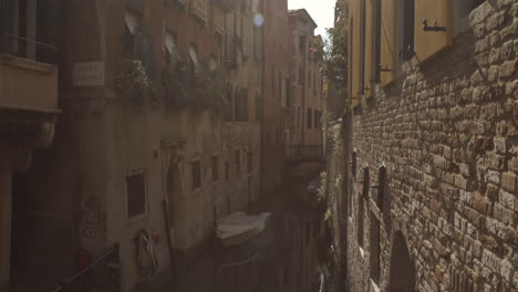 wide tilt up shot of historic water canal street cale castagna with brick wall, sun flares lens, venice, italy