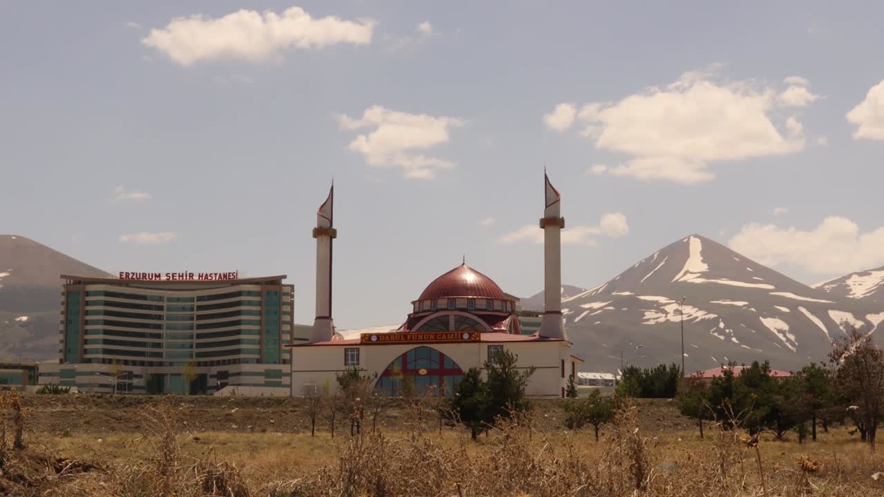 erzurum en turquía. 04.28.2021 hospital de erzurum, junto a una mezquita. en el fondo hay una montaña cubierta de nieve a finales de abril. turco: erzurum şehir hastanesi y darül fünun camii