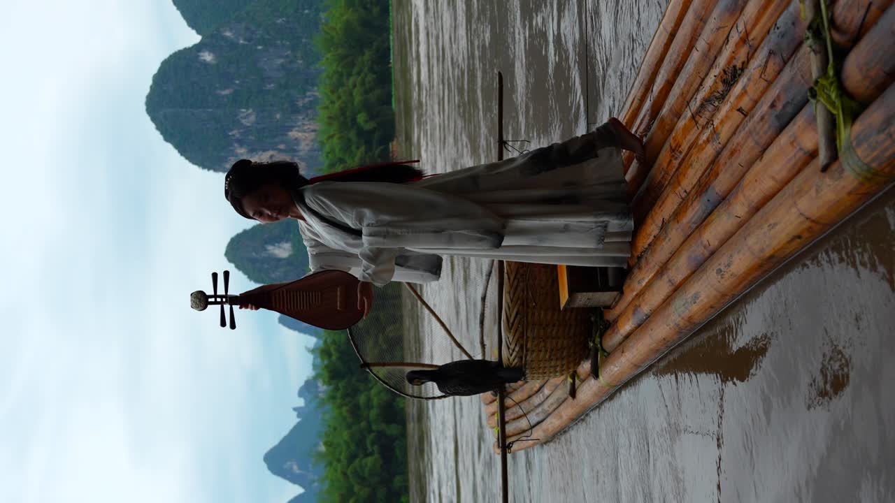 Ragazza Hanfu attraente in abiti tradizionali su zattera che tiene uno strumento a corda in Cina