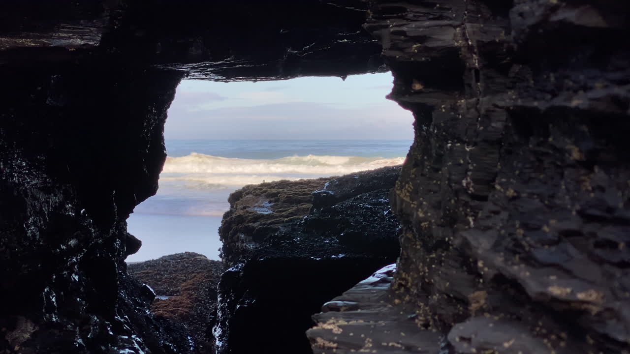 The sea reveals itself through a rocky window, waves framed by the dark stone of Sagres cliffs Black rocks crisscrossed by white mineral veins form patterns under the Atlantic light of Sagres