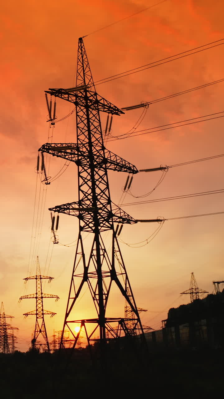 Tall electric towers at sunset. High voltage electric line distribute electricity through cables. Distribution station with metal pylons in the evening. Slow motion. Vertical video