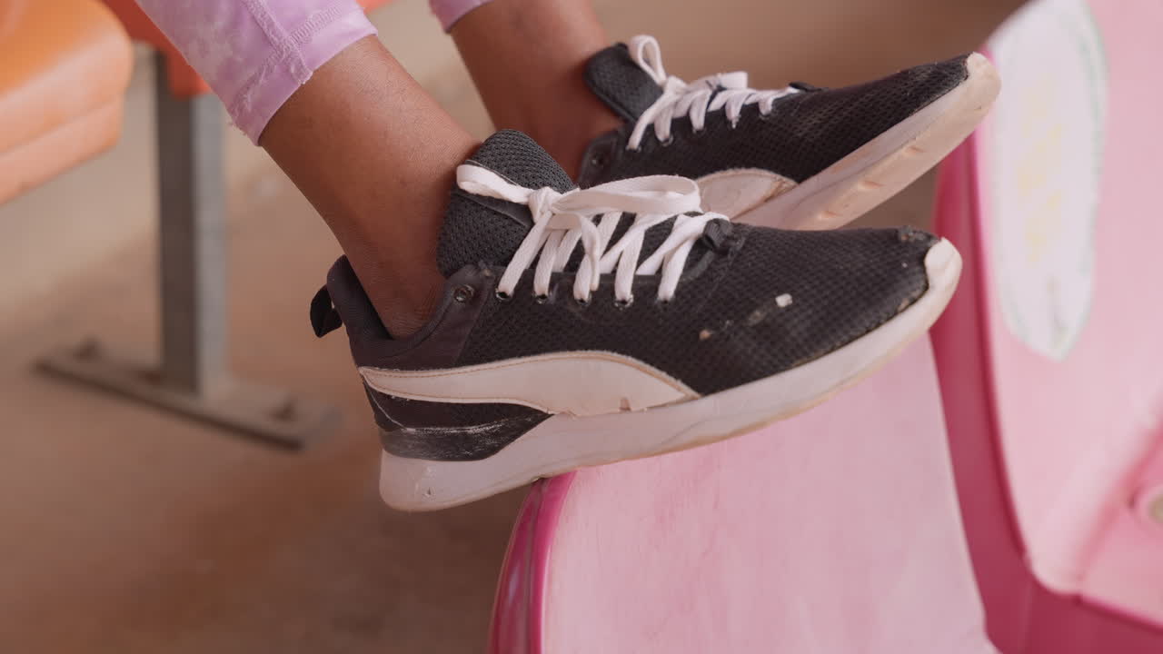 Campo largo di sneakers nere su sedili a gradinata rosa, leggings color lavanda, atmosfera casual da streetwear con una giocosa oscillazione della gamba, toni pastello caldi, lacci bianchi e suola testurizzata, atmosfera di un luogo per spettatori.