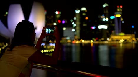 a woman is taking pictures of a night city on a smartphone