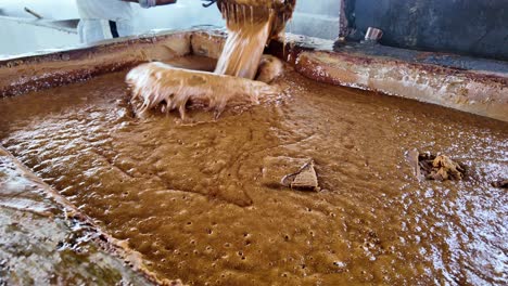traditional sugar cane processing: man scooping hot juice
