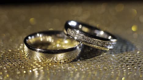 Wedding-rings-lying,-rotate,-spinning-on-shiny-golden-shining-surface-with-light,-close-up-macro