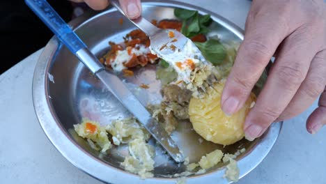 elderly female hand peeling boiled potato with fork then mashes it and mixes it with mashed carots