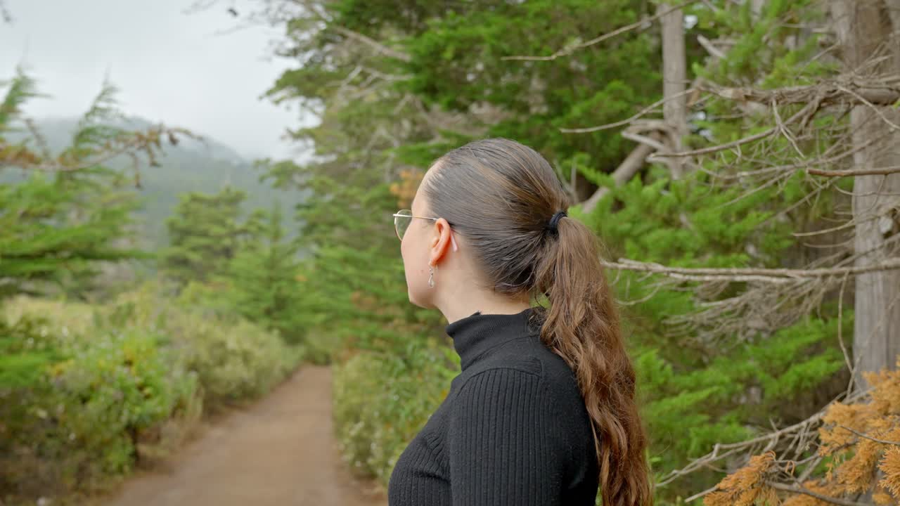Mujer joven con gafas disfruta de la naturaleza mientras hace senderismo en un bosque.