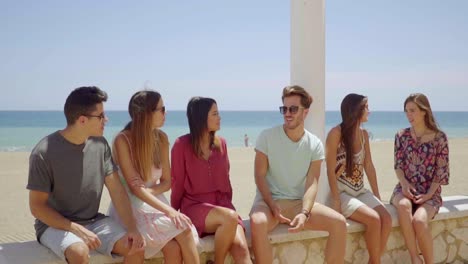 Group-of-friends-sitting-on-stone-wall-near-beach