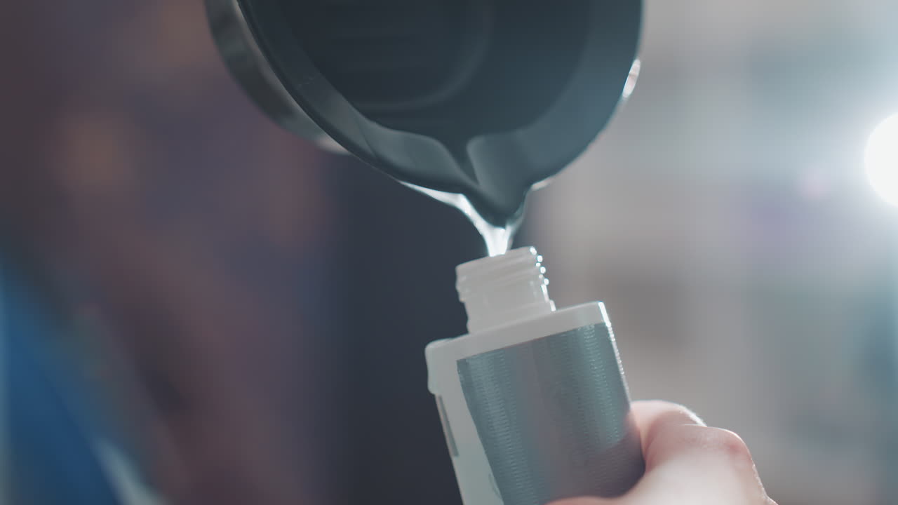 병에 천천히 따르는 시네마틱한 장면, 윤기 있는 액체가 리본처럼 흐르는 모습, 극적인 역광과 보케, 병을 조심스럽게 잡고 있는 손, 반사되는 표면, 프리미엄 제품 촬영을 위한 에디토리얼한 살롱 분위기