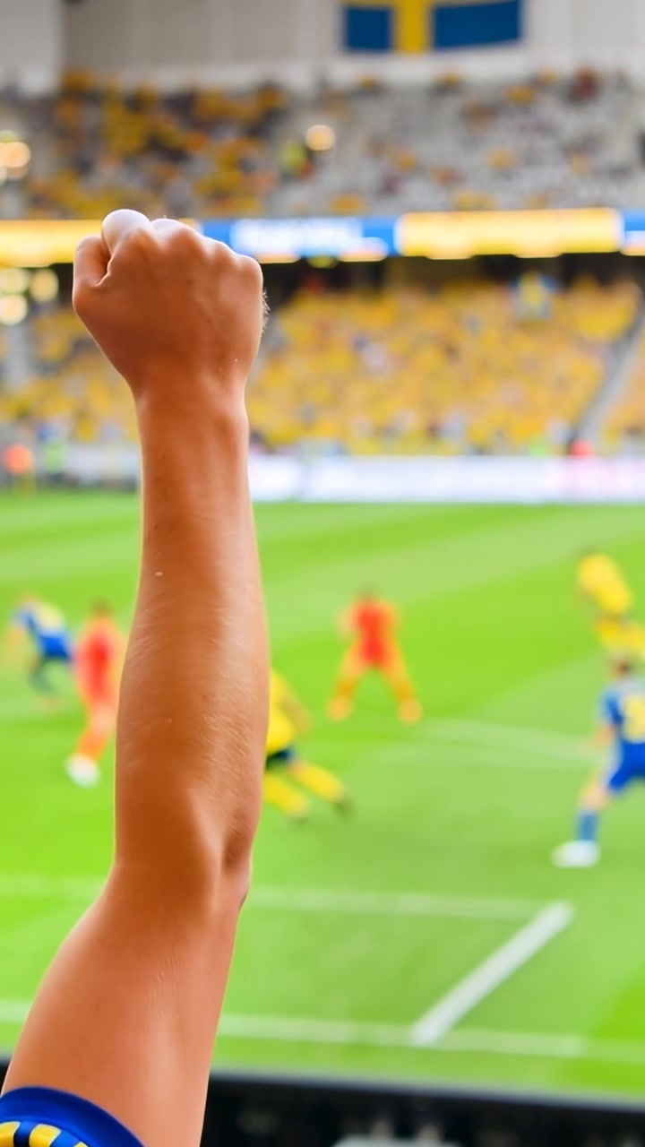 Video verticale: Tifoso che alza le braccia con una maglia gialla, agita i pugni sugli spalti reagendo a un'occasione da gol.