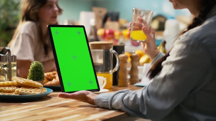 Pystysuuntainen chroma key -tabletti perheen kanssa aamiaista tarjoilemassa aurinkoisessa keittiössä