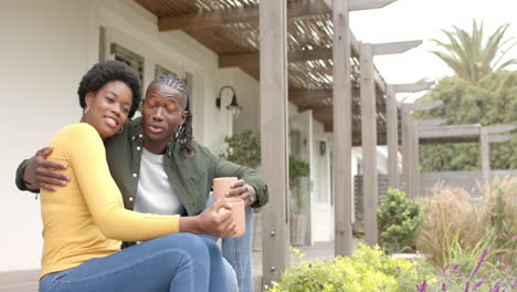 african american couple sitting on porch, embracing and enjoying coffee together at home