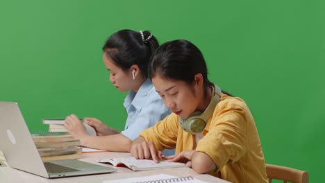 asian woman students reading books while sitting on a table with laptop in the green screen background classroom