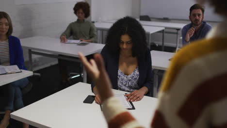 Mixed-race-colleuagues-sitting-during-presentation-in-meeting-room-making-notes