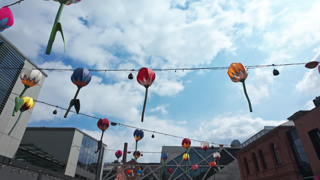 Colorful paper flower decorations hanging between buildings with a bright sky in Stara Praga, Warsaw