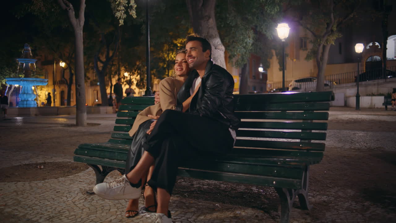 Affectionate couple sitting park cuddling in evening date. Happy spouses resting