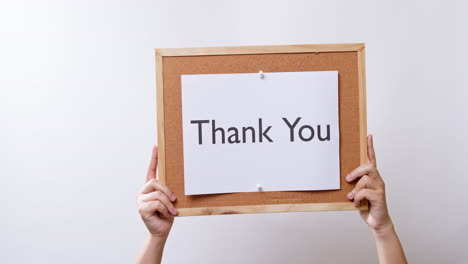 woman's hand shows the paper on board with the word thank you in white studio background with copy space