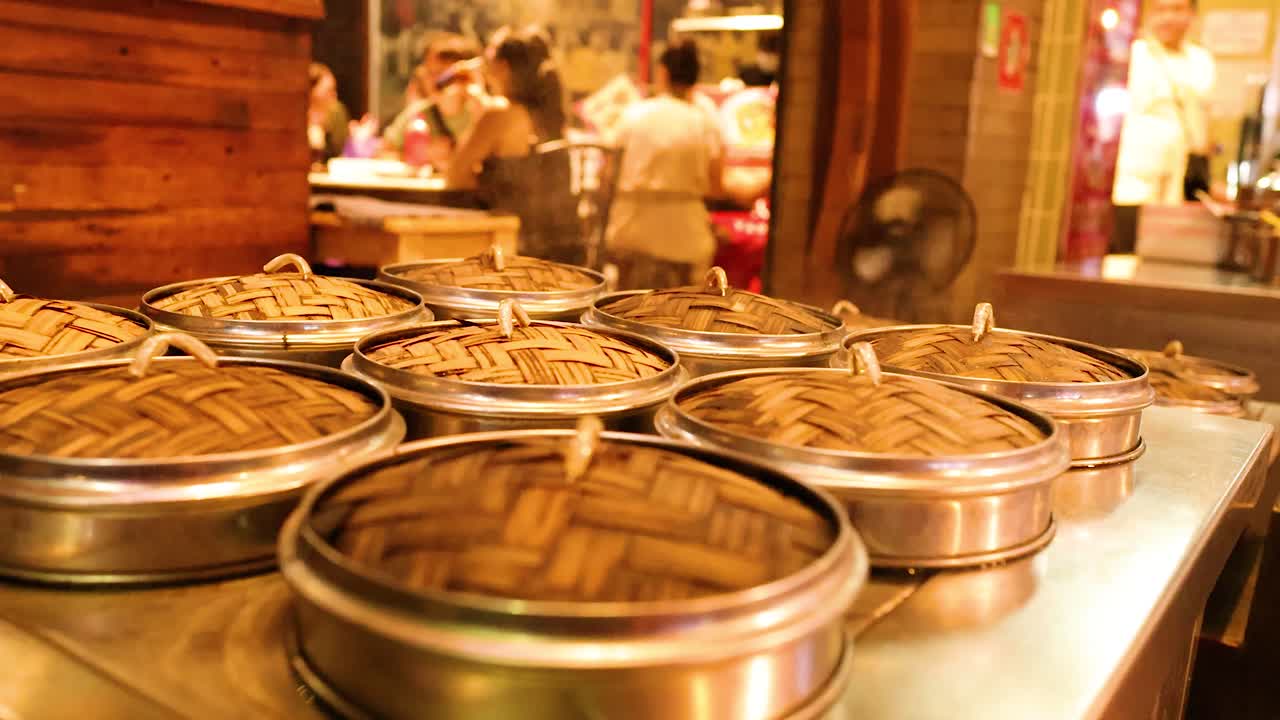 Bamboo steamers filled with dim sum on metal counter, warm lighting, busy night market background