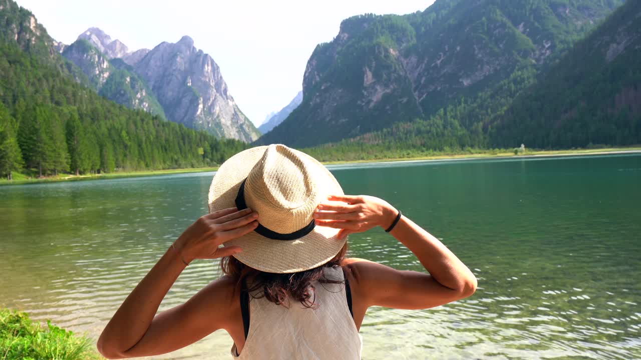 Turis memegang topi jeraminya menikmati pemandangan Danau Dobbiaco di Dolomites