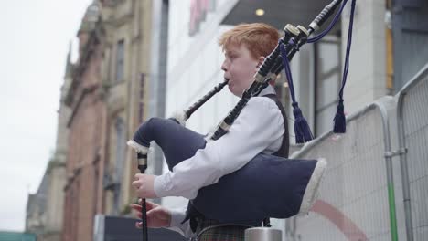 Young-man-wearing-tartan-is-playing-bag-pipes-outside-large-buildings