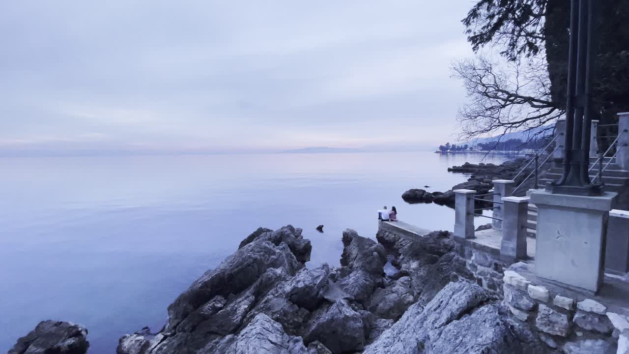 Para siedząca na brzegu morza z wyspą w oddali, szerokokątne ujęcie typu rybie oko, Lovran, Opatija, Chorwacja