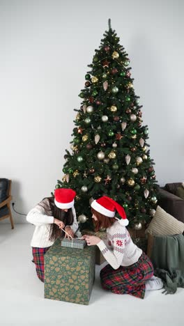 hermanas abriendo regalos de navidad cerca de un árbol de navidad