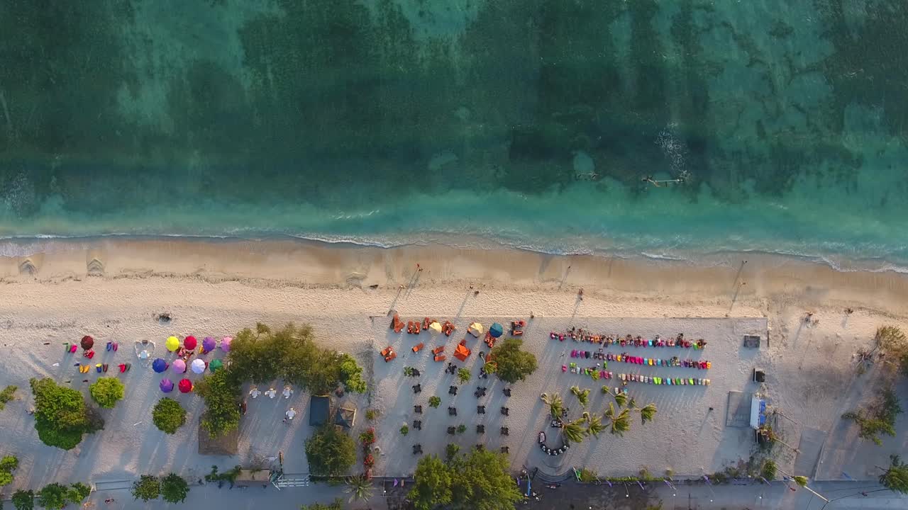 Vista aerea dall'alto dell'isola spiaggia di Gili Trawangan al tramonto, pouf e ombrelloni sulla spiaggia sabbiosa, persone che guardano il tramonto e si godono la vacanza.