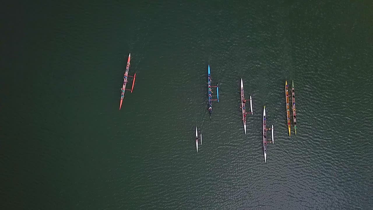 Aerial top down view above colourful teams of athletes in long rowing boats on lake