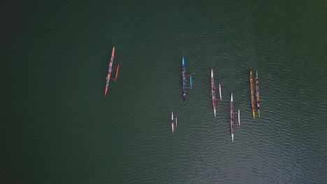 aerial top down view above colourful teams of athletes in long rowing boats on lake