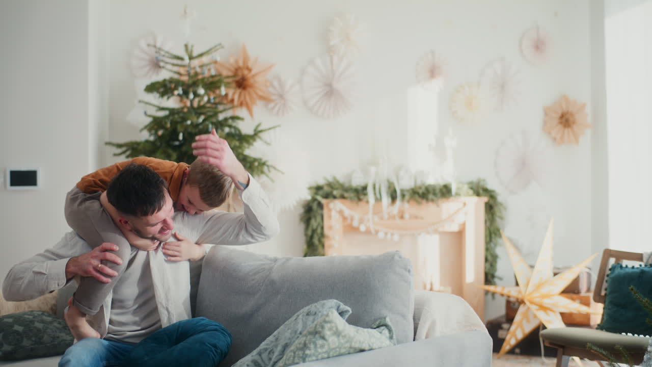 아들과 함께 휴가를 즐기고 있는 어린 소년은 아버지의 등 위에 뛰어다니며 기하며 소파에서 즐거움을 누리고 있다.