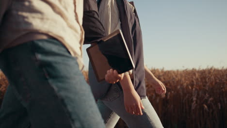 Farm-workers-walk-wheat-farmland.-Unknown-agronomist-hands-hold-tablet-closeup.