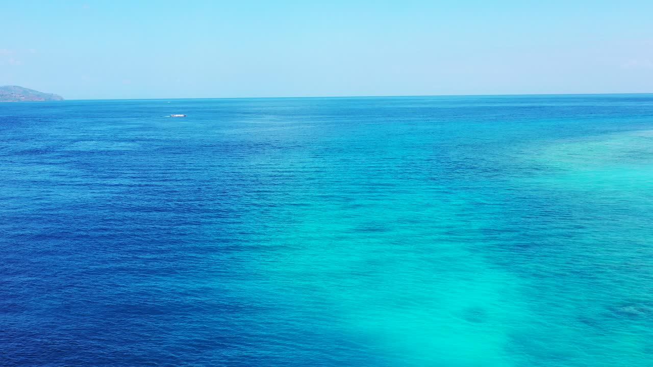 Flying over the beautiful tropical sea in Thailand, coral reef, crystal clear seawater and fishing boat drifting in front of the island in the distance