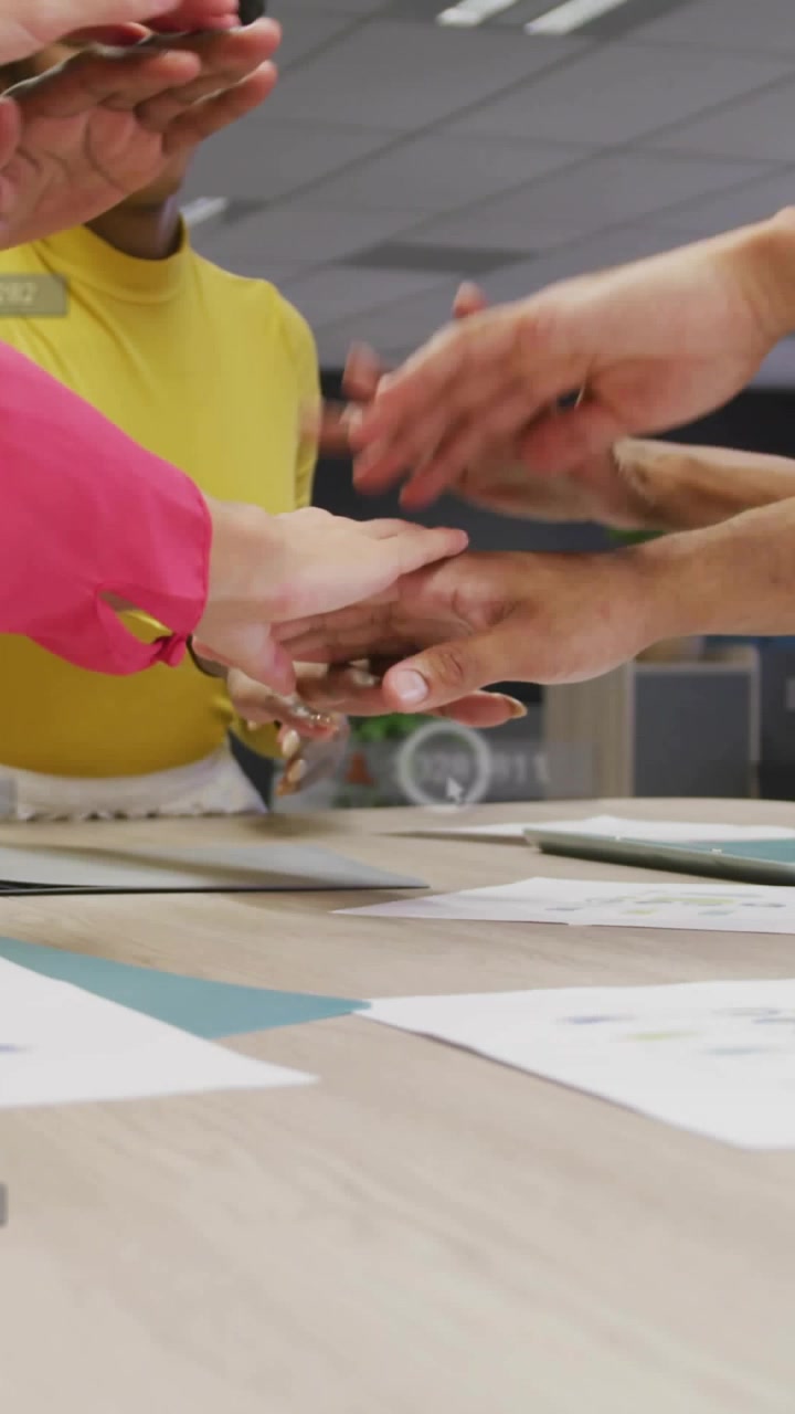 Video verticale: Un team impila le mani su un tavolo, generando sovrapposizioni animate che segnalano l'unità aziendale.