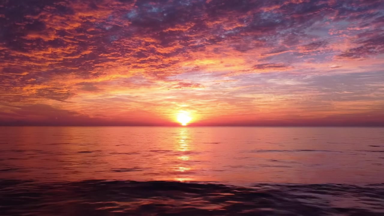 Atemberaubender Sonnenuntergang über ruhigem Ozeanwasser, der den Himmel mit atemberaubenden Orange-, Rosa- und Lilatönen erleuchtet, während der Tag in die Nacht übergeht.