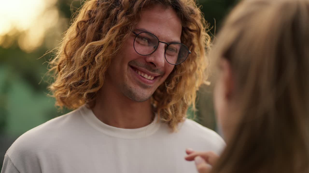 pov: un feliz chico de cabello rizado con una camiseta blanca y gafas está hablando con su novia