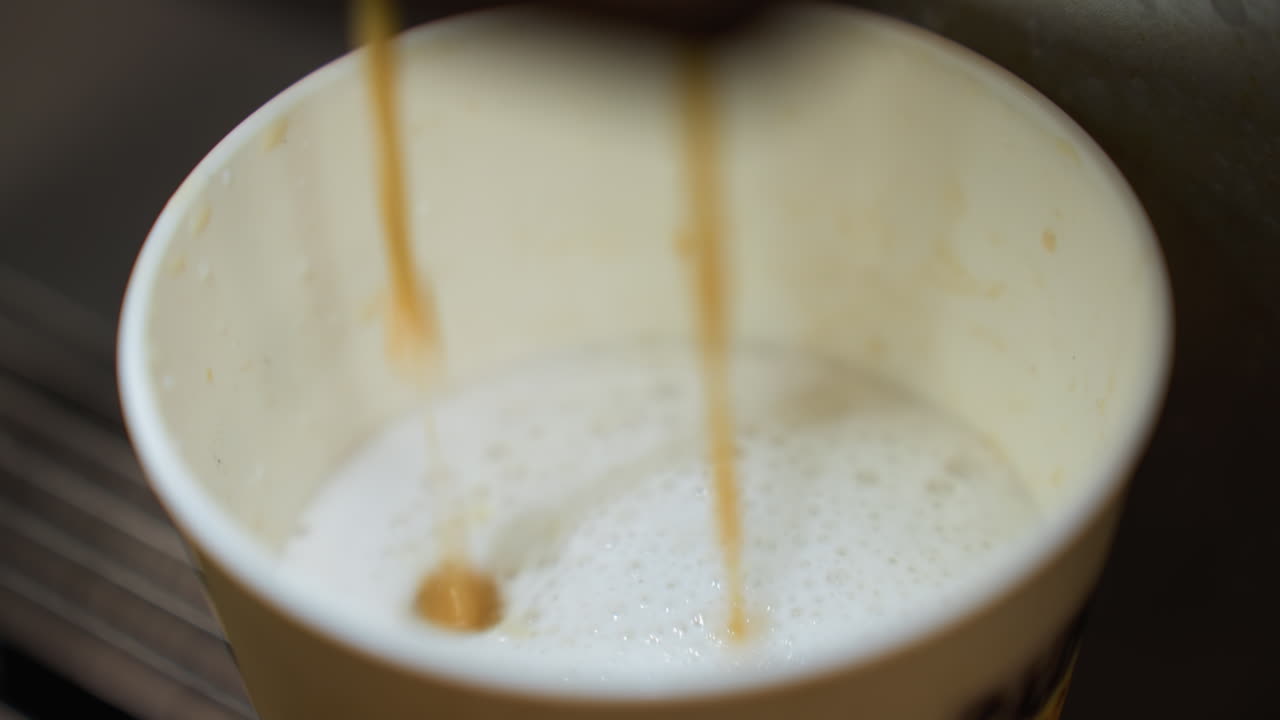 coffee pouring into a cup from a coffee machine. The video captures the detailed view of the coffee stream blending with the frothy milk in the cup, highlighting the process of coffee preparation
