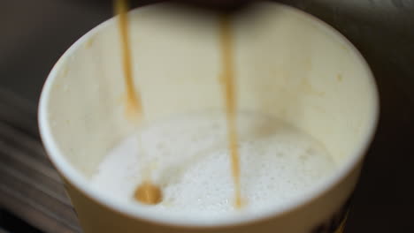 coffee pouring into a cup from a coffee machine. the video captures the detailed view of the coffee stream blending with the frothy milk in the cup, highlighting the process of coffee preparation