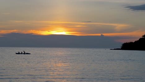 tourists in a rowboat at colorful orange sunset, silhouettes against the setting sun