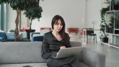 Eine-Junge,-Schöne-Frau-Im-Anzug-Erzählt-Und-Spricht-Fröhlich-Per-Videoanruf-über-Einen-Laptop,-Während-Sie-In-Einem-Business-Center-Sitzt