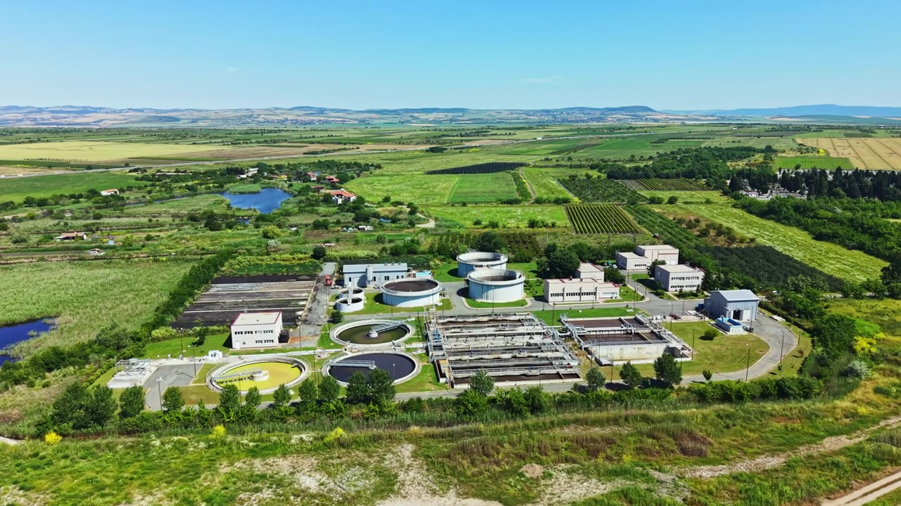 View of a water treatment facility surrounded by fields and hills on a sunny day in a rural area