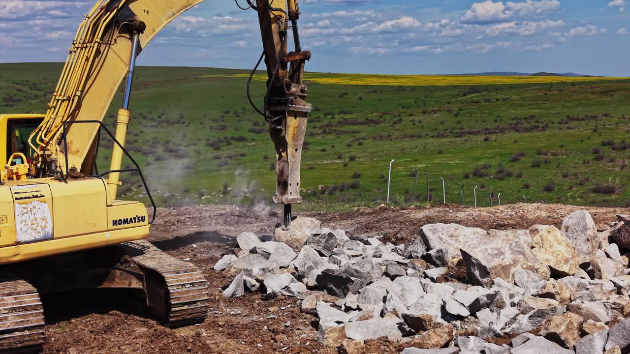 Construction equipment breaks rocks on a hillside in a rural area