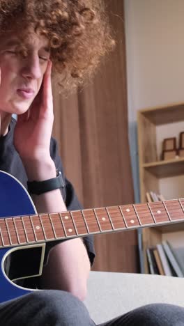 a young curly-haired musician with a guitar plays a calm sad melody. the young guitarist is tired.