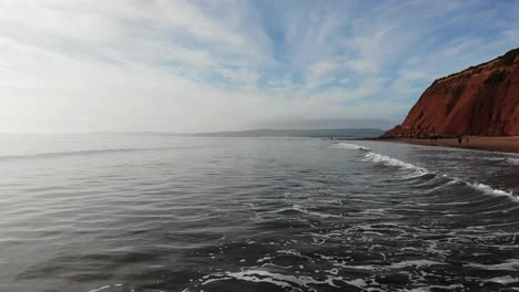 Antena-Volando-Bajo-Sobre-Las-Olas-Al-Lado-De-La-Playa-De-Orcombe-Point