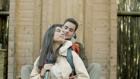 young couple sitting at wooden house porch in forest